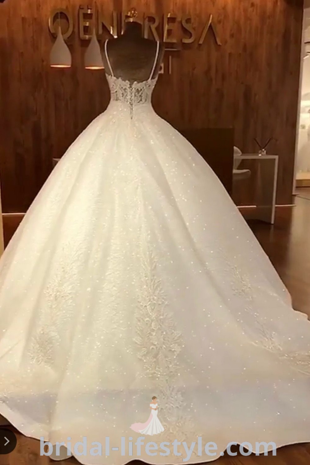 An elegant white wedding dress displayed in front of a sign reading queeneaa, showcasing bridal trends and romantic designs for dreamy brides. This ball gown captures the essence of wedding dresses, offering charming inspiration for the special day at bridal-lifestyle.com.