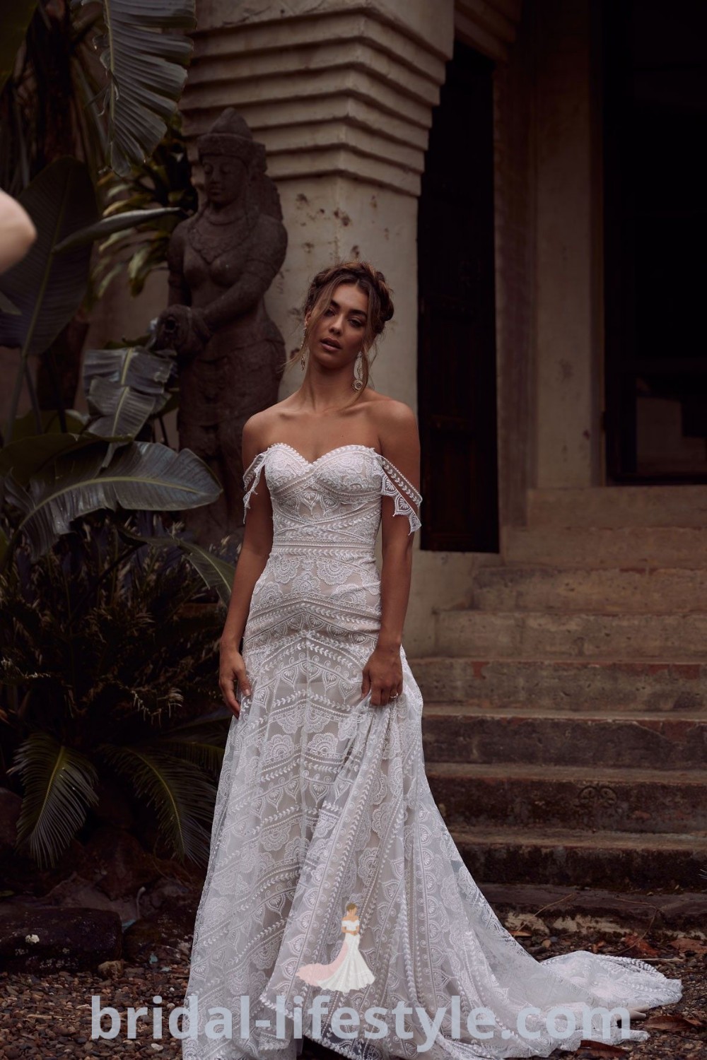 A woman in a Boho Off The Shoulder Wedding Dress stands gracefully on steps, showcasing the contemporary bridal style and elegance. This gown is perfect for beach weddings and dreamy brides, offering the best aesthetic ideas. Discover more at bridal-lifestyle.com.