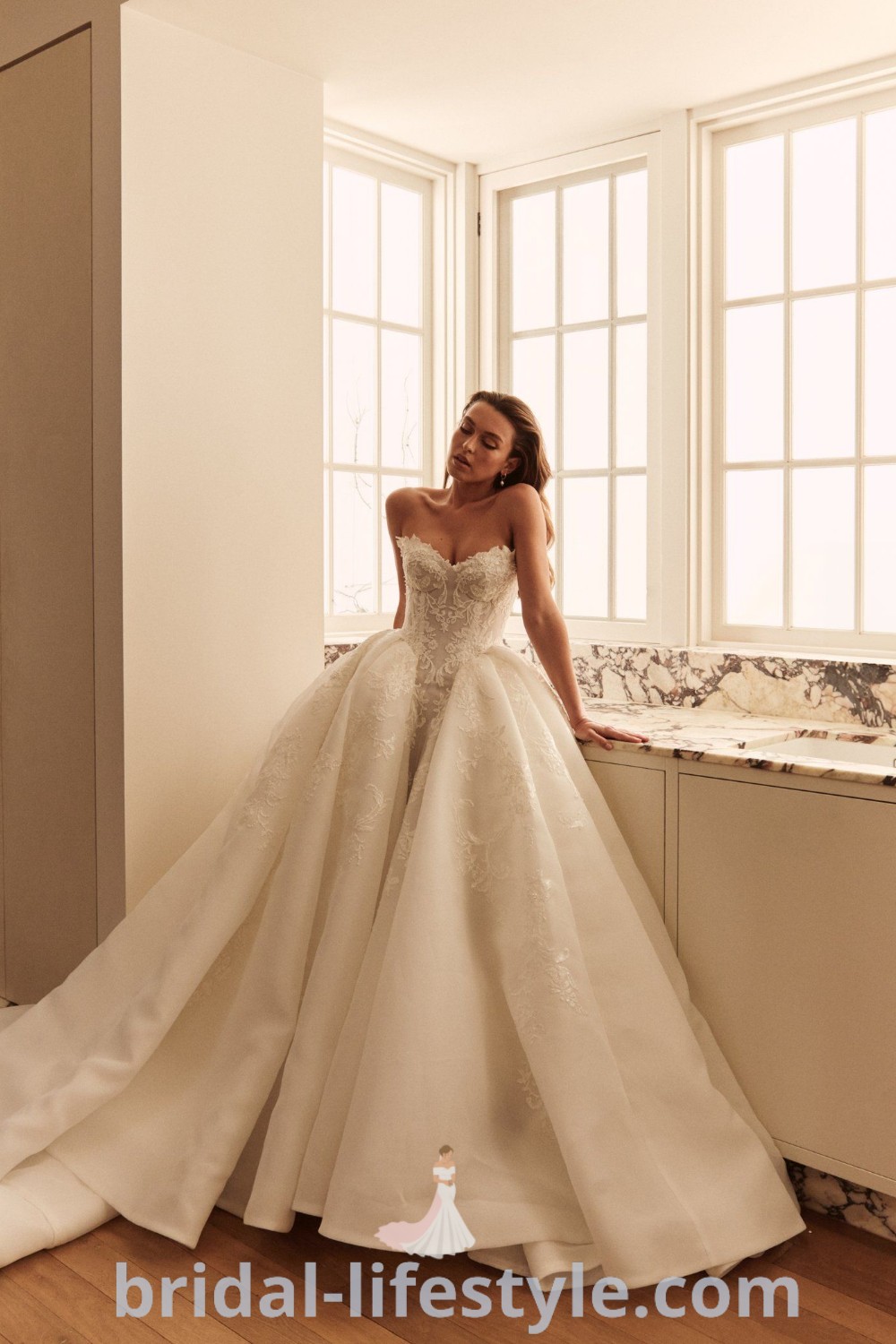 A woman in a wedding dress leaning against a window, showcasing a beautiful silk ballgown, ideal for elegant brides seeking dreamy inspiration. This image highlights the best wedding dress trends, including poofy and big ballgown styles. Find your perfect look at bridal-lifestyle.com.