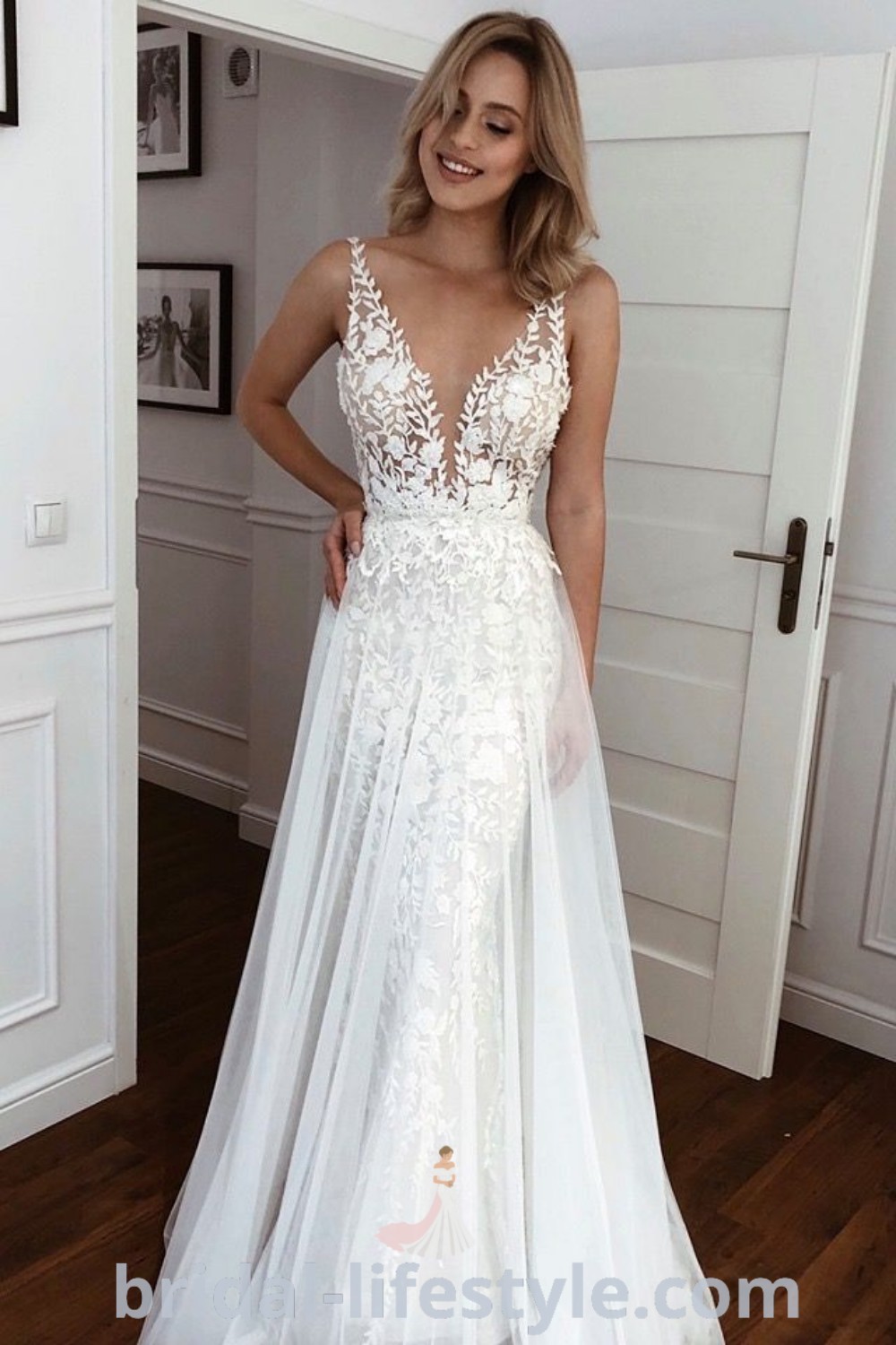 An elegant woman in a 2in1 wedding dress stands on a wooden floor, showcasing a stylish look for beach weddings and vow renewals. This sleeveless design offers dreamy inspiration for brides seeking the best aesthetic ideas for their special day, found at bridal-lifestyle.com.