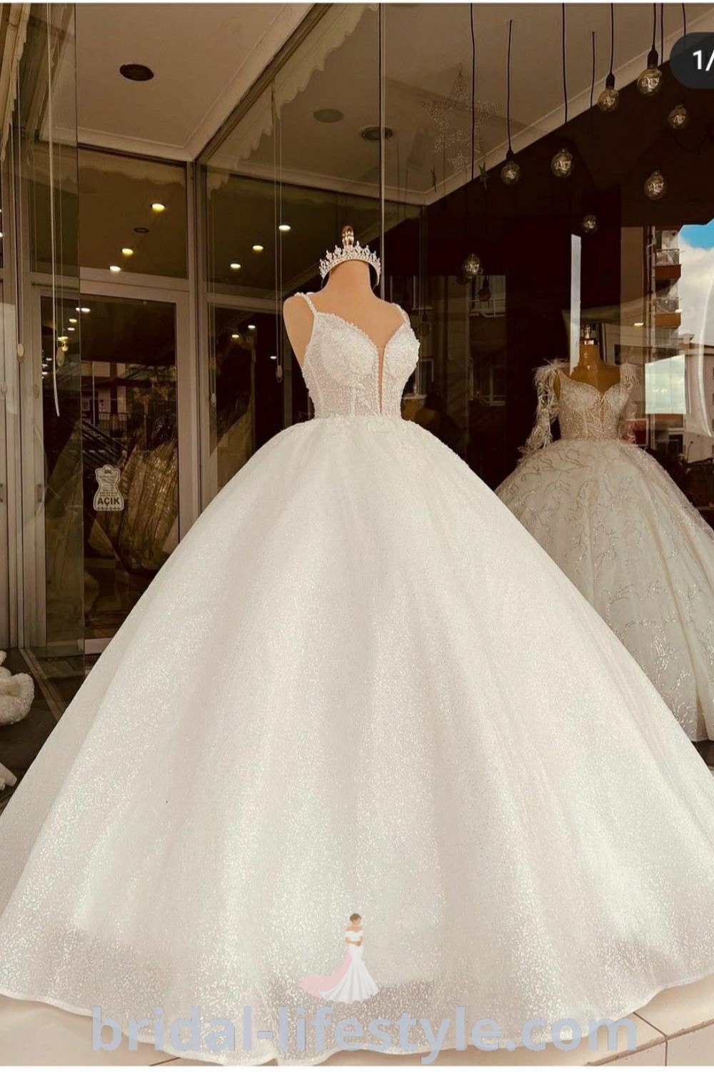 An elegant white wedding dress showcased in a store window, with stylish mannequins behind it, ideal for brides discovering the best trends and fabrics for their special day. Explore romantic and dreamy designs at bridal-lifestyle.com.