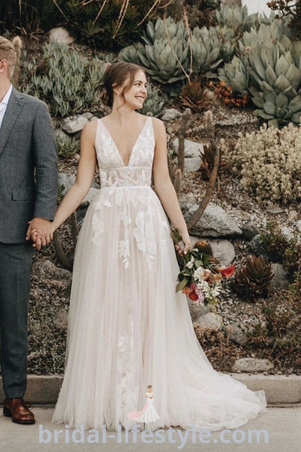 A bride and groom holding hands in front of a cactus wall with succulents, showcasing a romantic A-line wedding dress made of tulle. The scene reflects boho wedding trends and offers inspiration for nature-inspired weddings. Discover the best aesthetic ideas and dresses of your dreams at bridal-lifestyle.com.