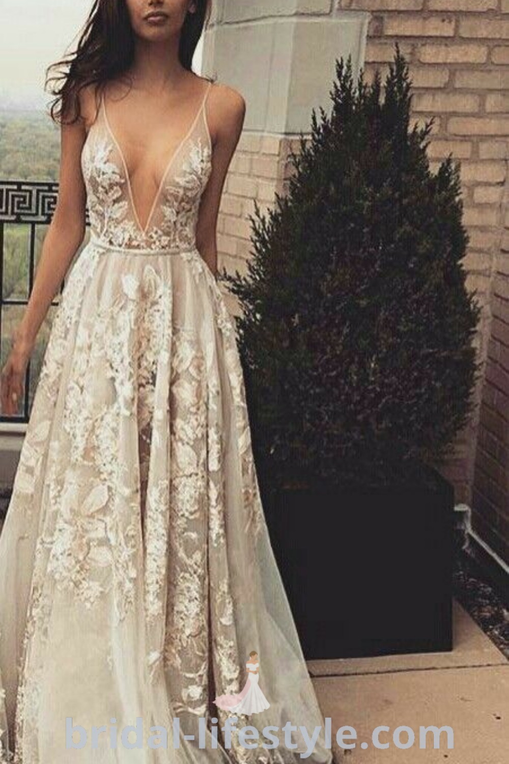 An elegant woman in a white dress stands on a balcony next to a building, showcasing the best wedding dress inspiration for brides. This classy attire captures dreamy trends and aesthetic ideas perfect for every bride