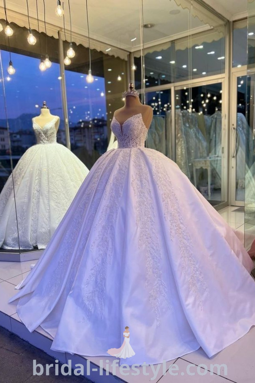 A display of elegant wedding gowns in a store window at night, adorned with lights that highlight Cinderella-style dresses, ballroom wedding dresses, and gorgeous princess ballgowns, offering inspiration for brides at bridal-lifestyle.com.