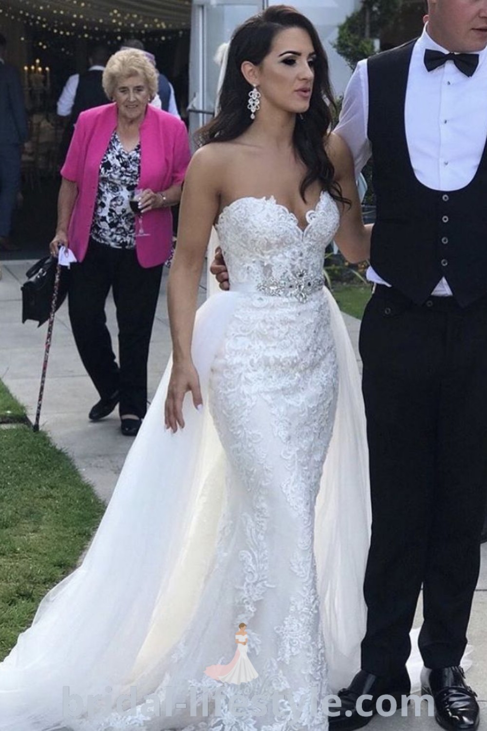 A bride and groom walking down the sidewalk, featuring a fitted wedding gown with detachable skirt, epitomizing the best aesthetic ideas for romantic weddings. This scene captures the elegance and charm that brides envision for their special day. Find inspiration for dresses of your dreams at bridal-lifestyle.com.