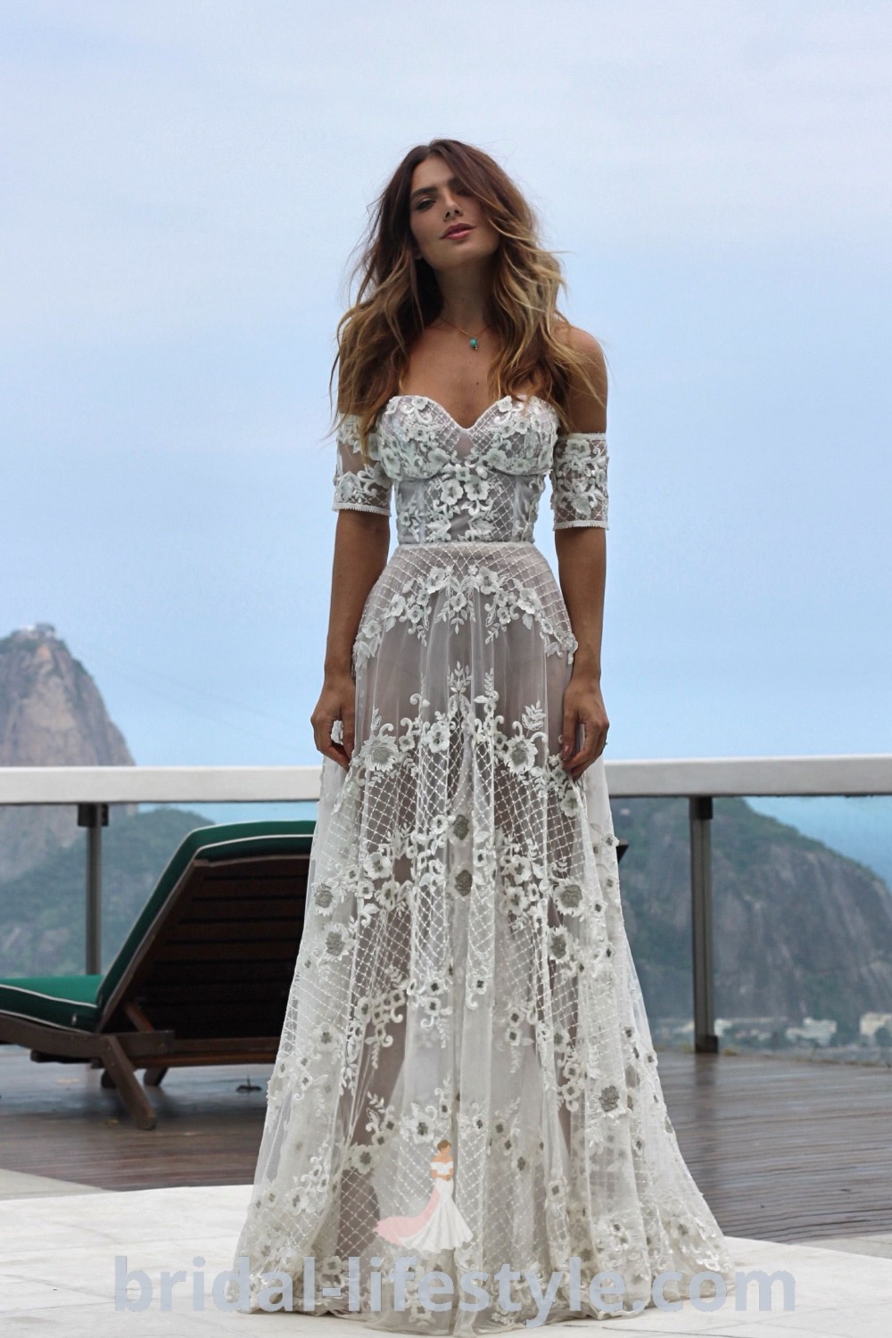 A woman in a white boho beach wedding dress standing on a balcony, embodying elegance and romance, showcasing trends for dreamy brides. Perfect for beachy weddings, this style offers inspiration for unique bridal looks. Explore more at bridal-lifestyle.com.