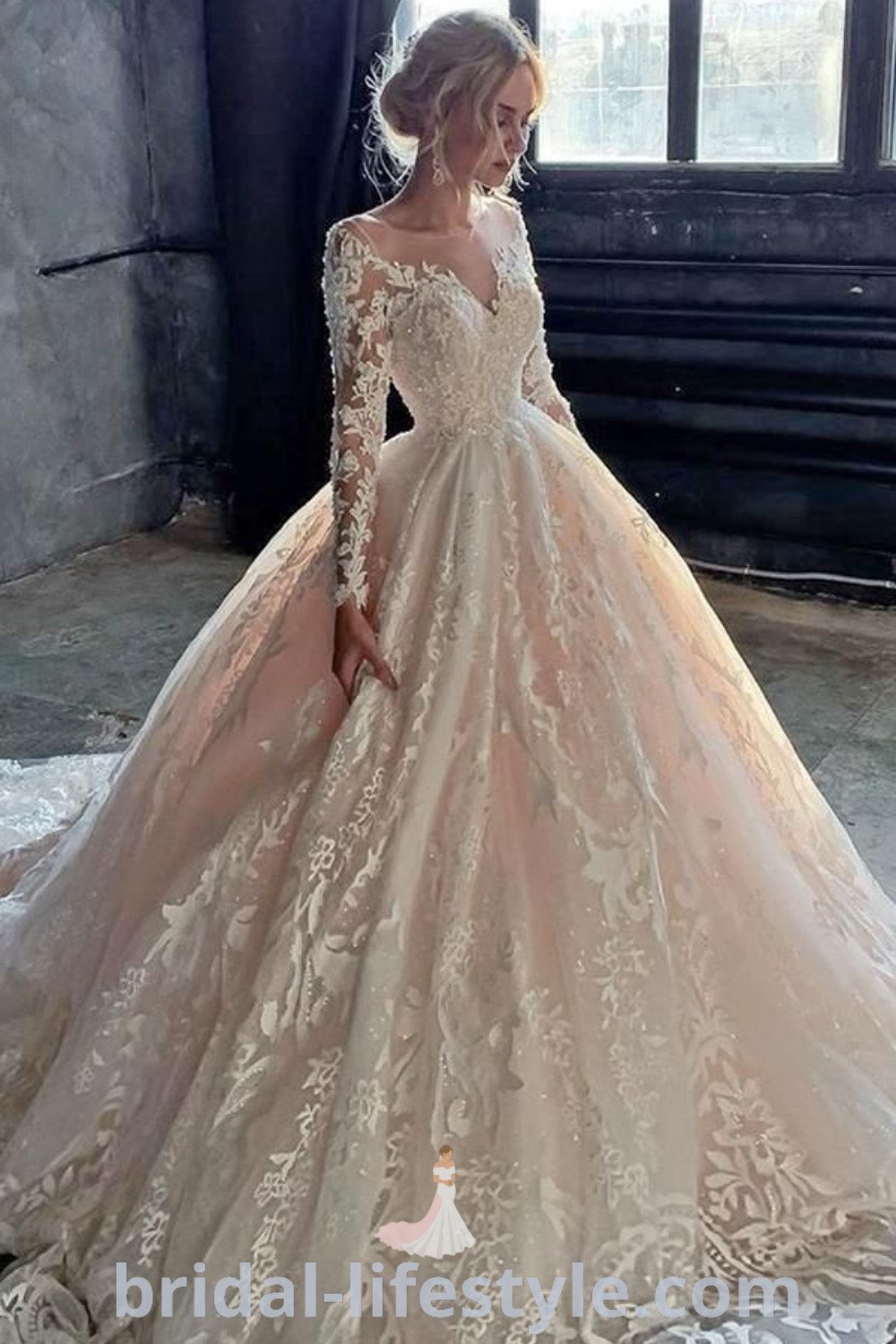 An elegant woman in a long sleeve wedding dress standing by a window, showcasing a lace ballgown that exemplifies romantic bridal trends. Perfect for every bride’s unique taste, this stunning dress from bridal-lifestyle.com is ideal for the special day.