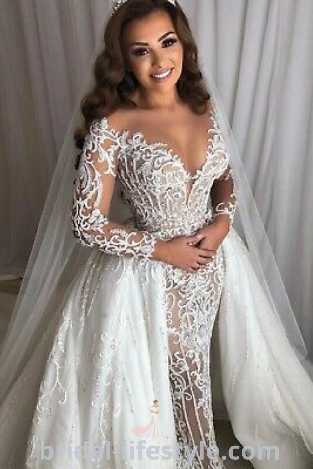 A woman in an elegant wedding gown and veil poses confidently, showcasing a stunning bridal look for the special day. This dress represents the best trends and aesthetic ideas for dreamy brides. Find more inspiration at bridal-lifestyle.com.