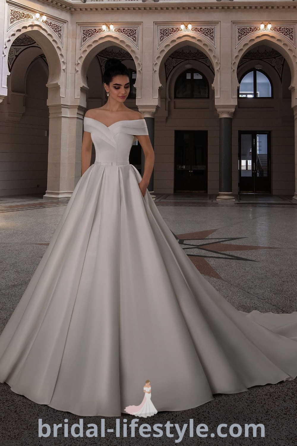 An elegant woman in a satin ball gown wedding dress stands in a large room adorned with columns and arches, showcasing the perfect balance of simplicity and sophistication. This unforgettable gown is an ideal choice for brides seeking dreamy styles. Discover more at bridal-lifestyle.com.