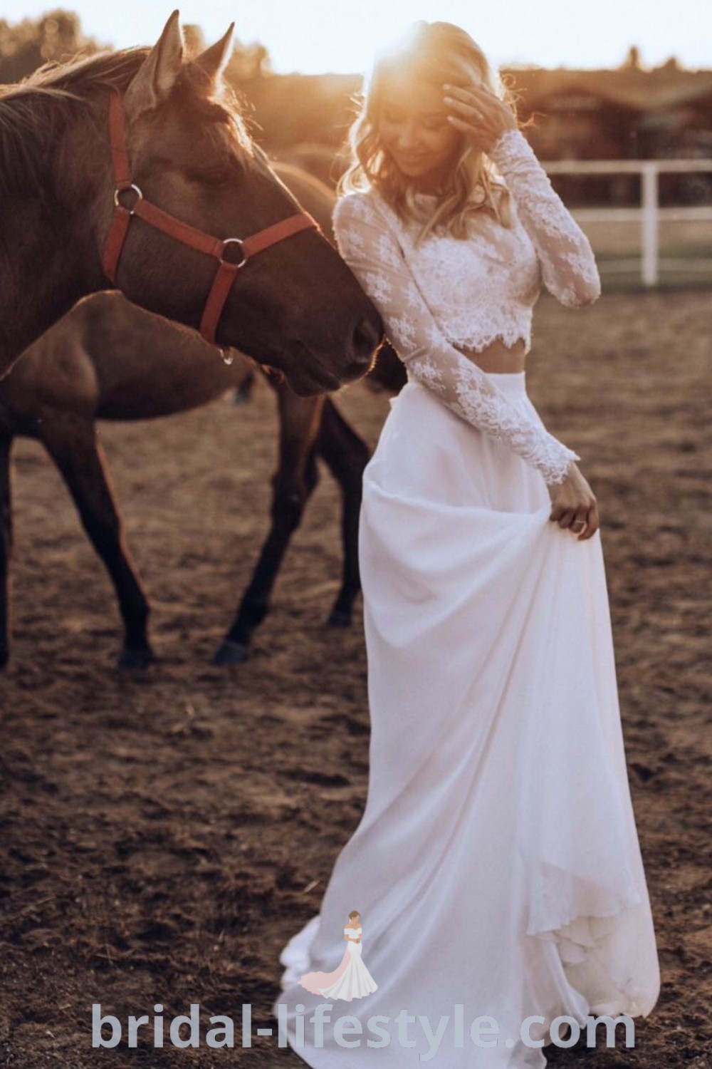 An elegant woman in a white two piece wedding dress stands next to a brown horse on a dirt field, showcasing trending bridal aesthetics perfect for prewedding shoots or receptions. Discover more inspiration for your special day at bridal-lifestyle.com.