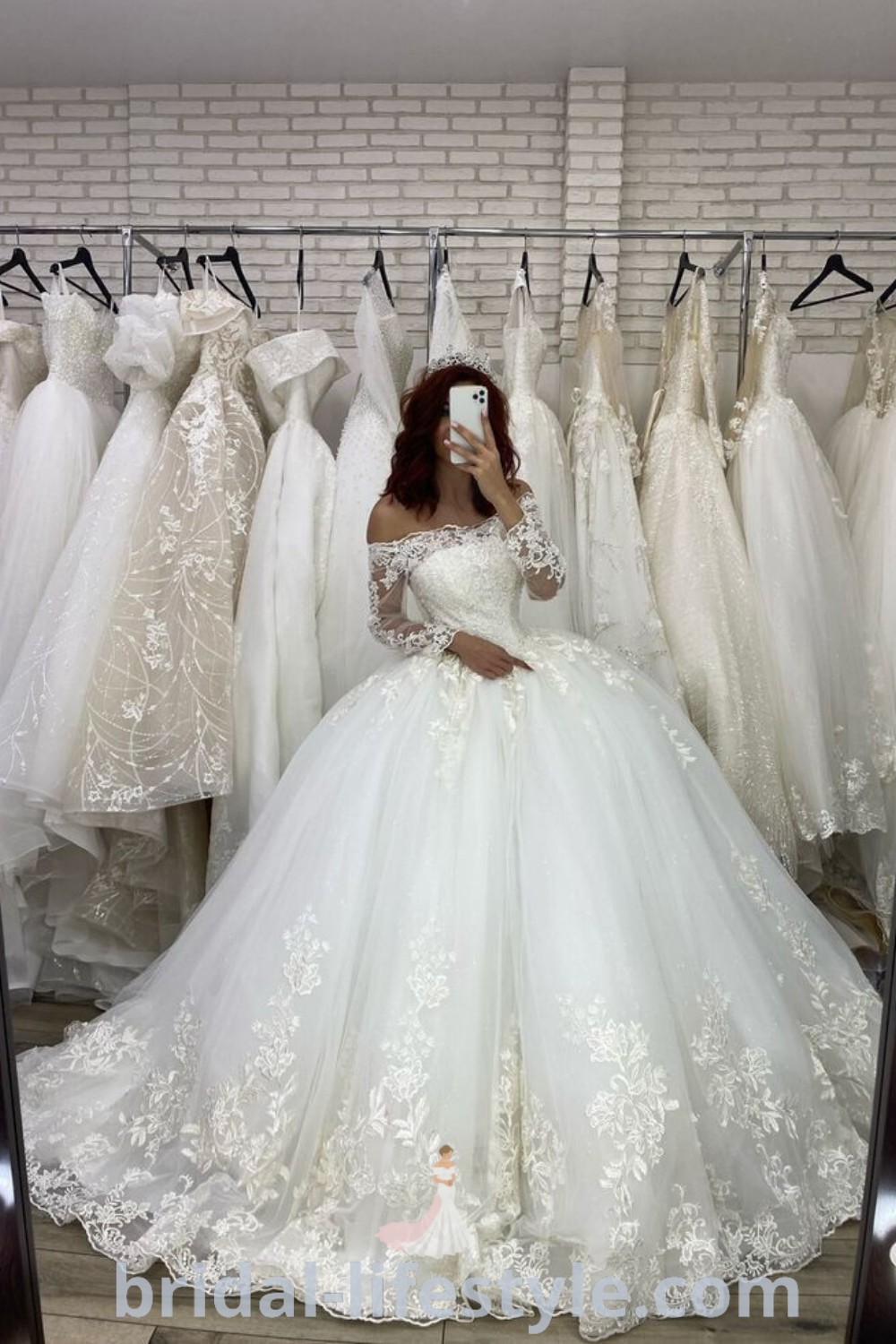 An elegant woman sitting in front of a mirror wearing a poofy wedding dress featuring fluffy details and an illusion neckline. This dreamy gown represents the best trends in wedding dresses for every bride
