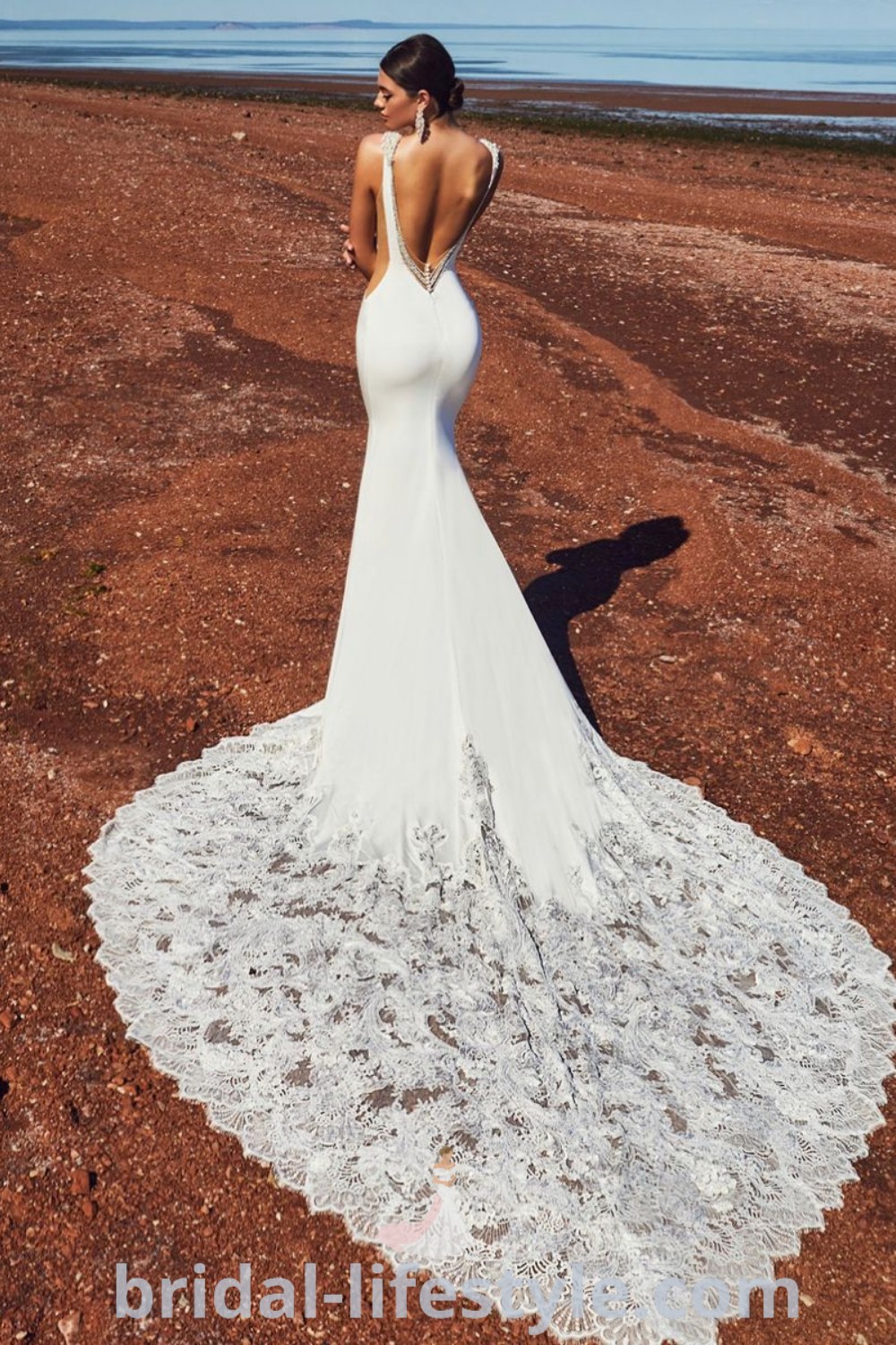 A woman in a white modern simple wedding dress stands gracefully on the beach, showcasing a backless mermaid silhouette from Calla Blanche. This elegant gown embodies romantic and sparkly elements, perfect for every bride