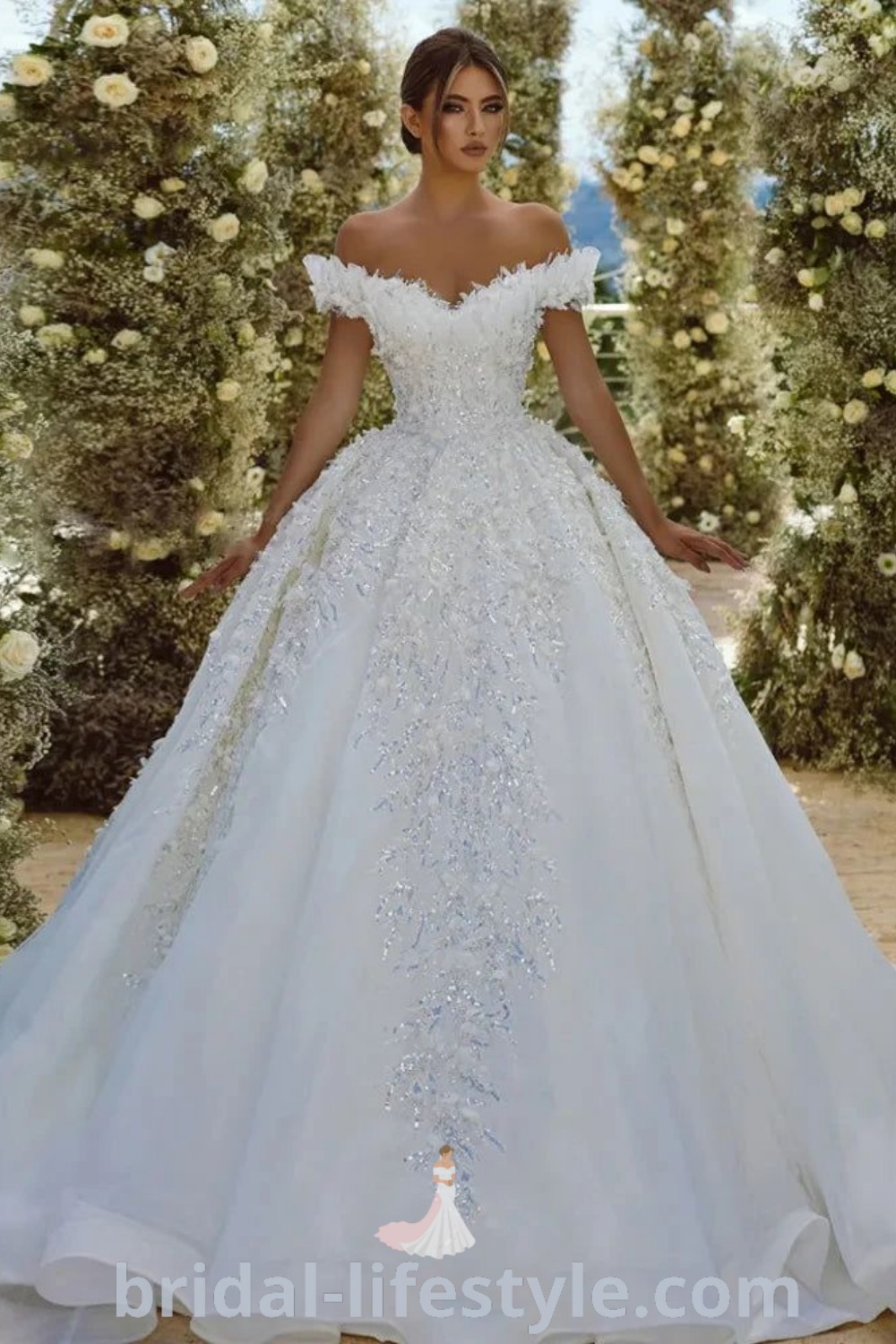 A woman in a white wedding dress stands next to colorful bushes and flowers, embodying elegance and romance for the special day. This image offers inspiration looks for brides and highlights the best aesthetic ideas. Discover more on bridal-lifestyle.com.