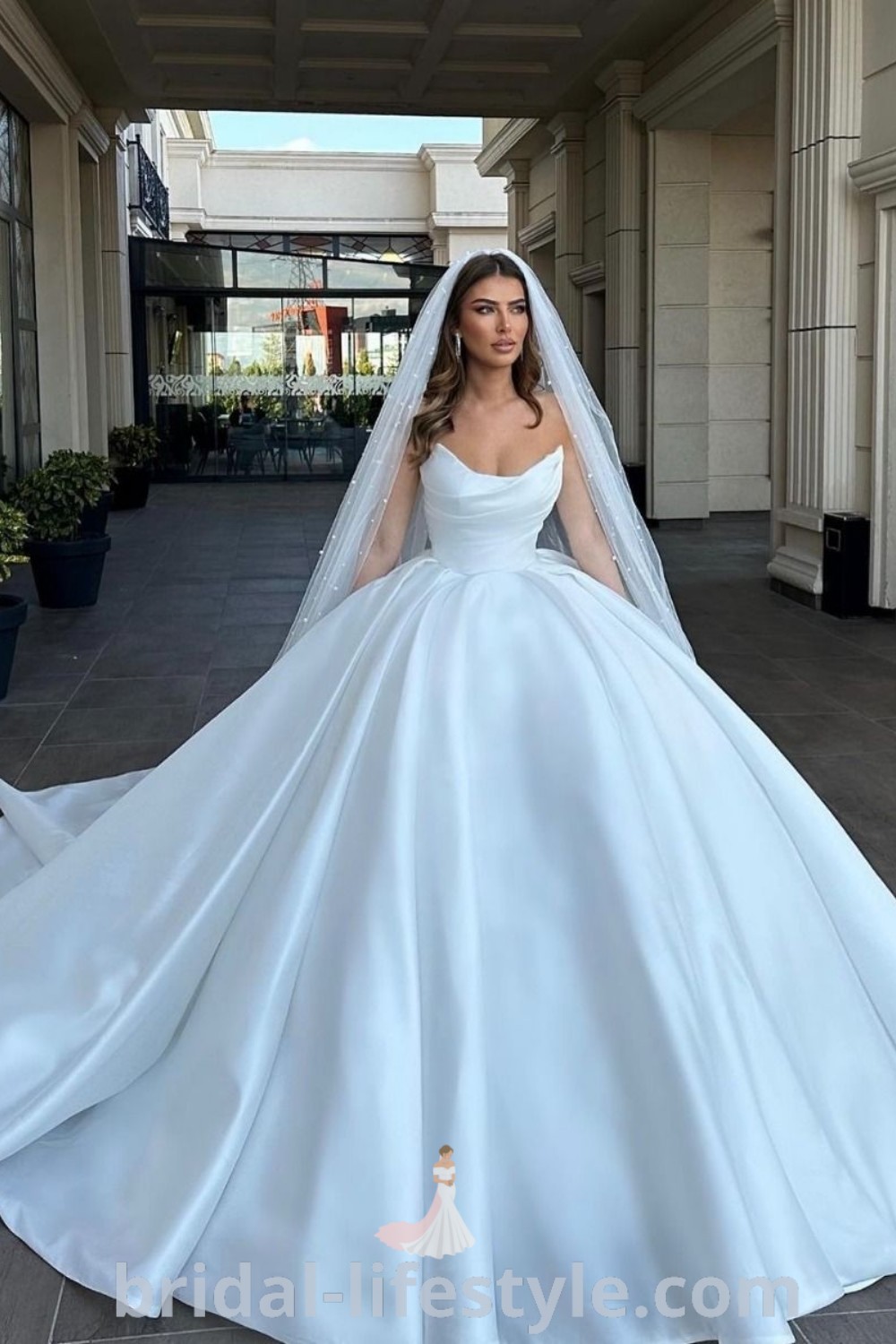 A woman in a satin wedding gown poses for the camera with her veil pulled back, showcasing the elegant design perfect for fall weddings. This dreamy bridal gown captures romantic moments and autumn vibes, making it a top choice for brides. Discover more at bridal-lifestyle.com.