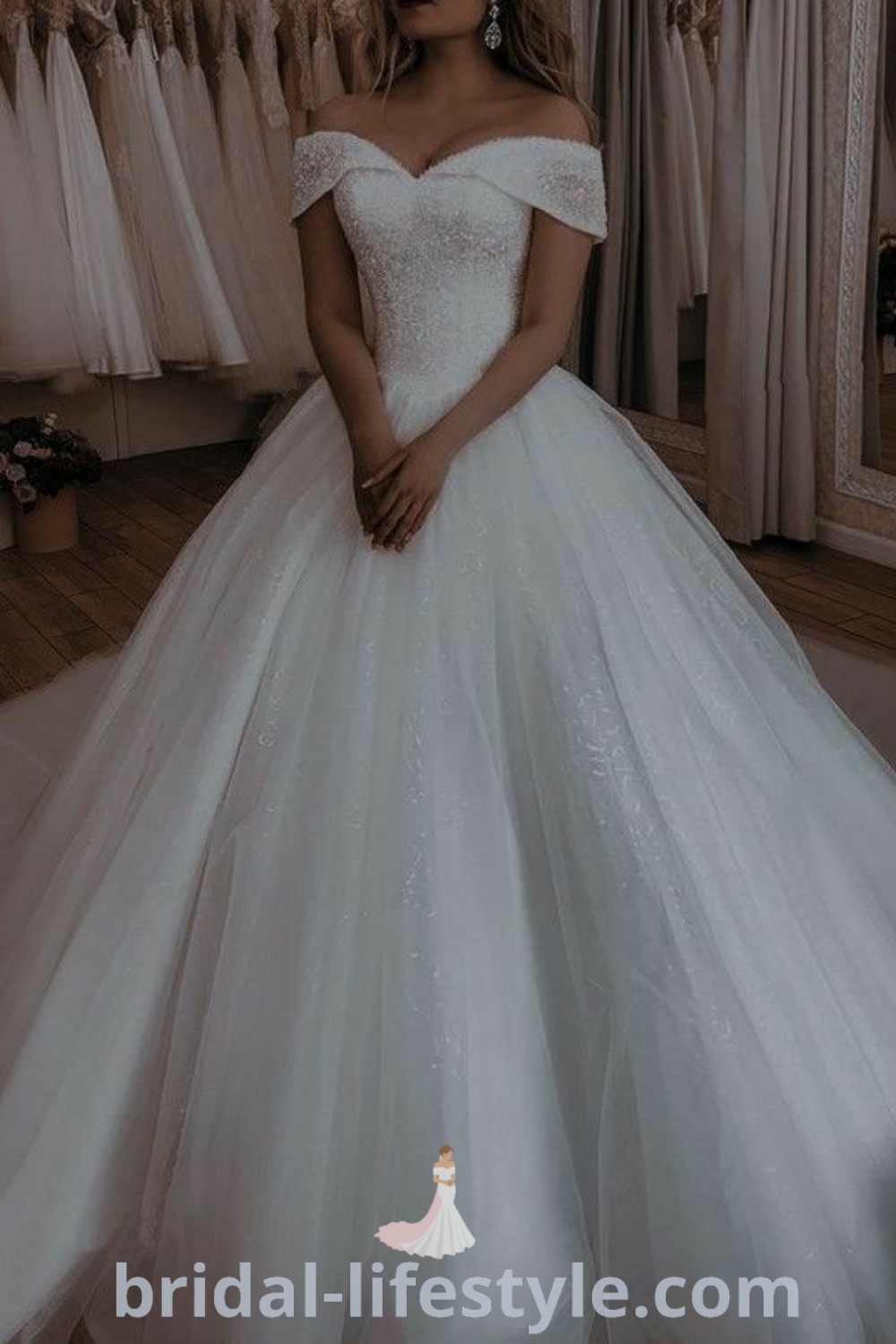 An elegant woman in a white wedding dress stands in front of a rack showcasing classy wedding dresses, reflecting the best aesthetic ideas for every bride’s unique taste. Discover pretty and fancy wedding dresses that inspire dreamy bridal looks at bridal-lifestyle.com.