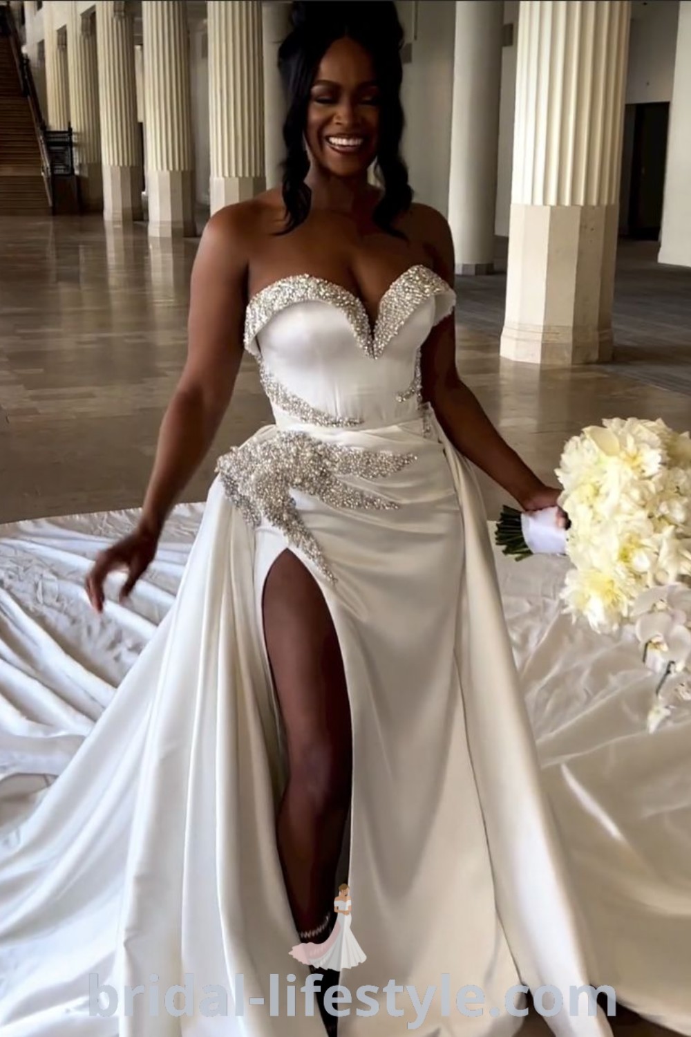 A woman in a white wedding dress poses elegantly for the camera, showcasing the sheer crystal design ideal for vow renewal and extravagant weddings. The gown exemplifies dreamy bridal trends, perfect for brides seeking inspiration looks for their special day. Discover more at bridal-lifestyle.com.