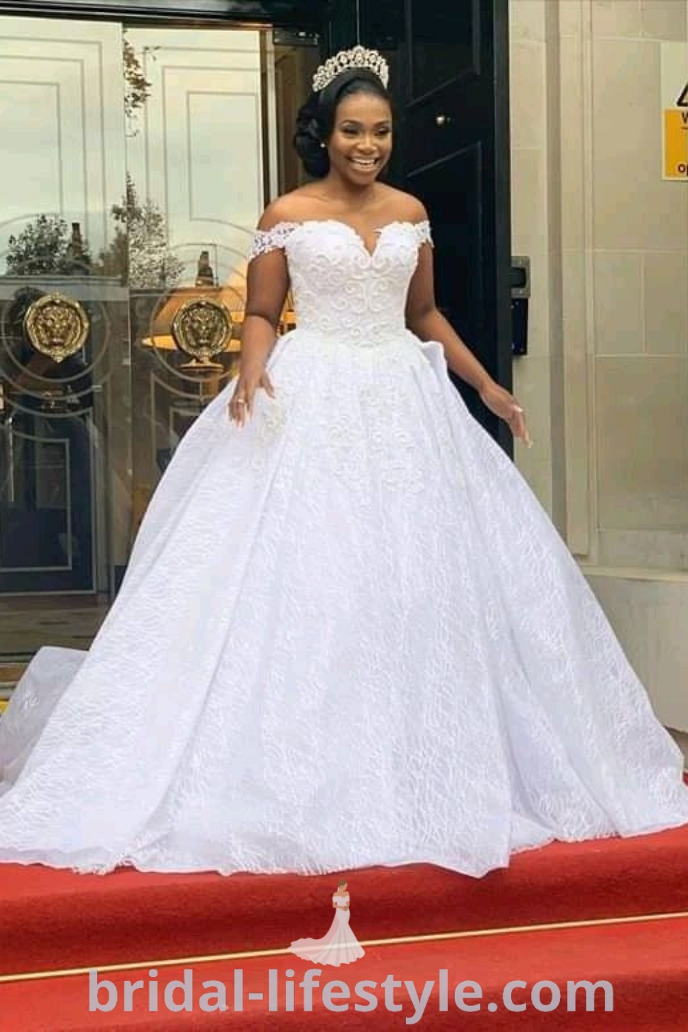 An elegant woman in a white lace wedding dress stands on the red carpet, perfect for black weddings, showcasing the best aesthetic ideas for dreamy brides. Discover more inspiration for your special day at bridal-lifestyle.com.