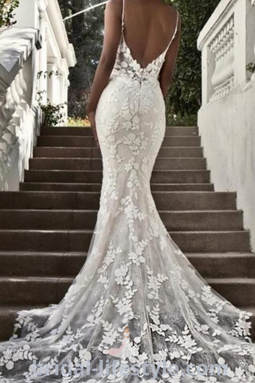 An elegant Enzoani Blue wedding dress with an open back, floral appliques, and a sheer lace mermaid silhouette. This backless fishtail style is perfect for brides looking for romantic and trendy dresses for their special day. Discover more wedding inspirations at bridal-lifestyle.com.