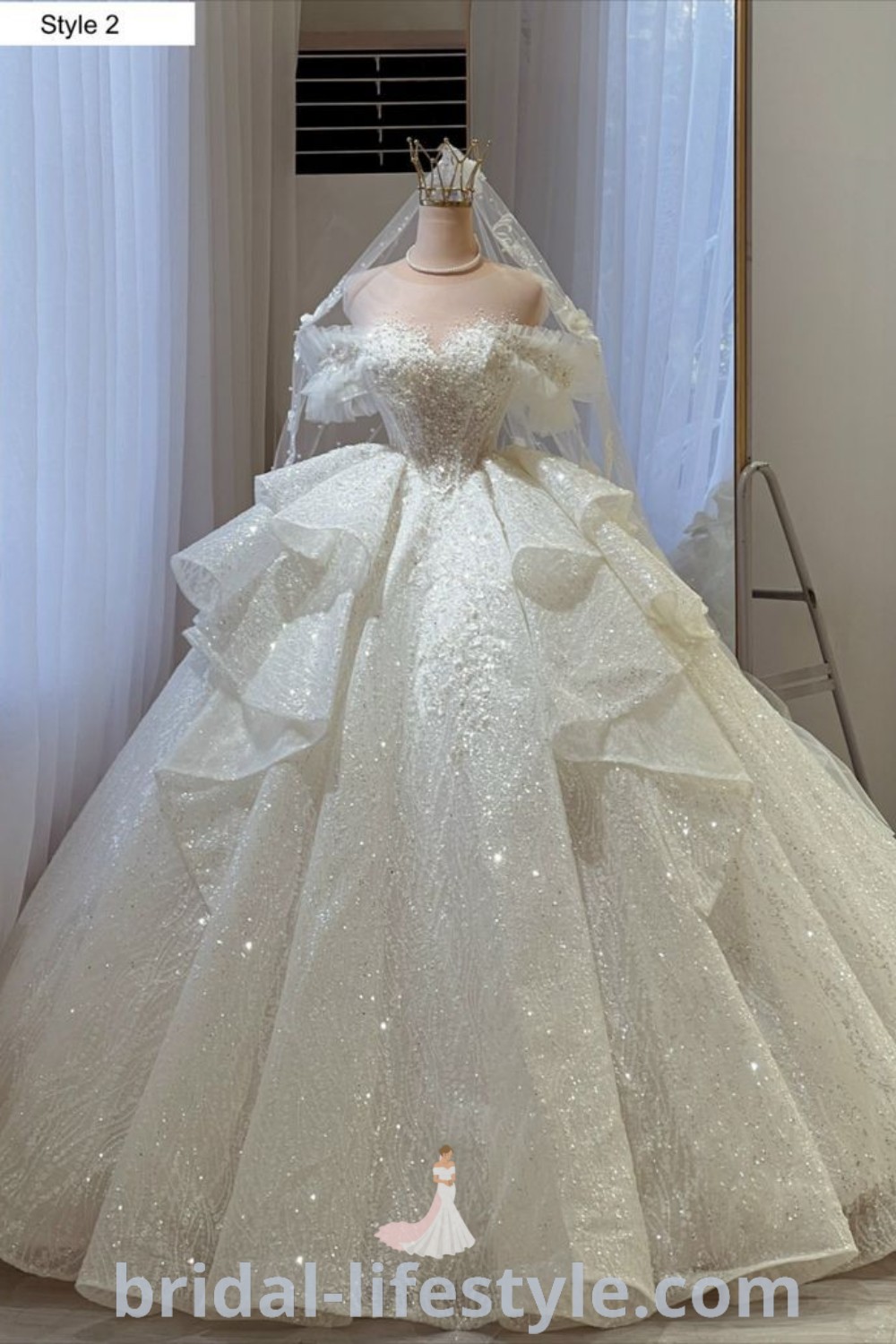 An elegant white wedding dress on display in front of a window, featuring off the shoulder sleeves and a fluffy ball gown design, ideal for romantic weddings. Discover the best inspiration looks and bridal trends at bridal-lifestyle.com.