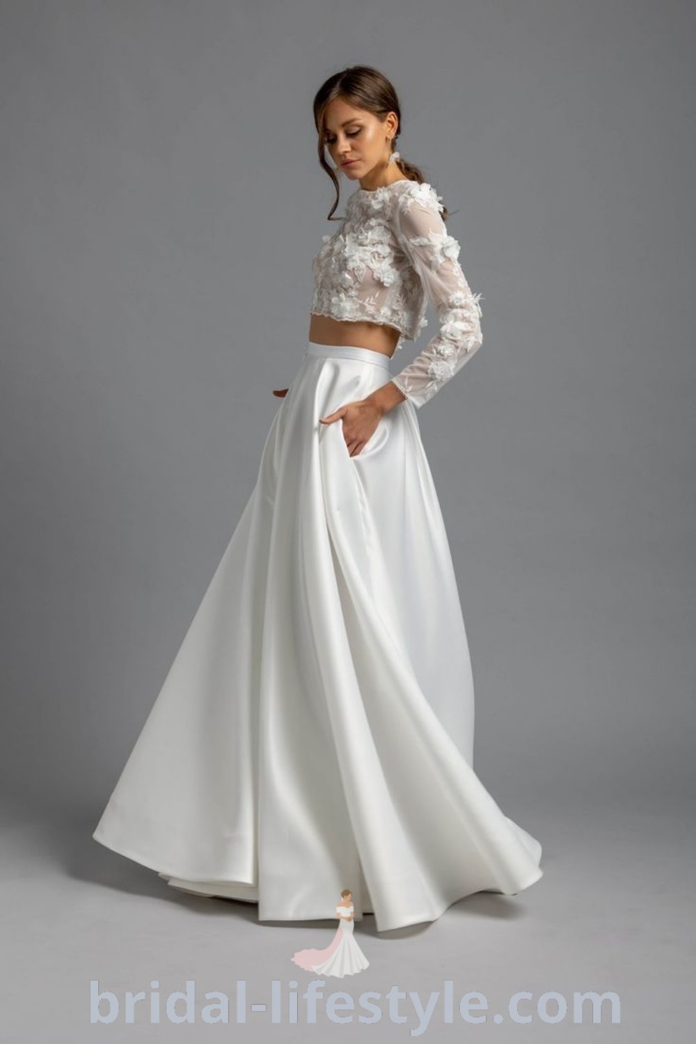 An elegant woman in a white dress with a long skirt and top, perfect for bridal occasions. This lovely long sleeve crop top is a trend for dreamy brides and offers aesthetic ideas inspired by bridal-lifestyle.com.