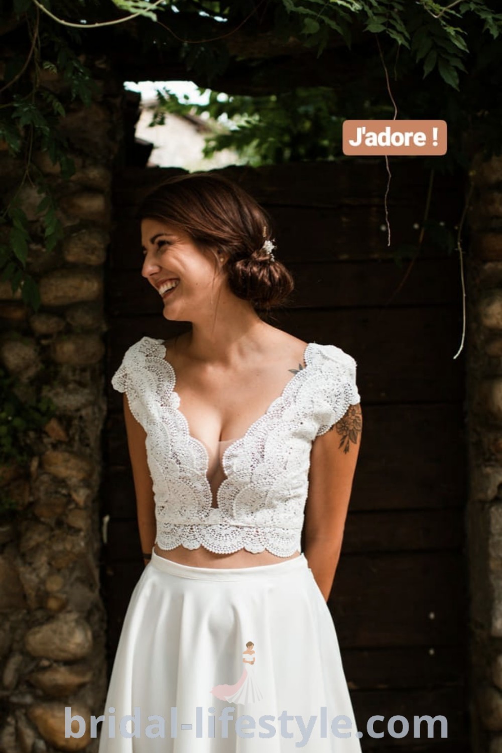 A woman standing in front of a stone wall wearing a white skirt and crop top, showcasing an elegant boho wedding dress two-piece that is perfect for romantic mountain weddings. Discover more at bridal-lifestyle.com.