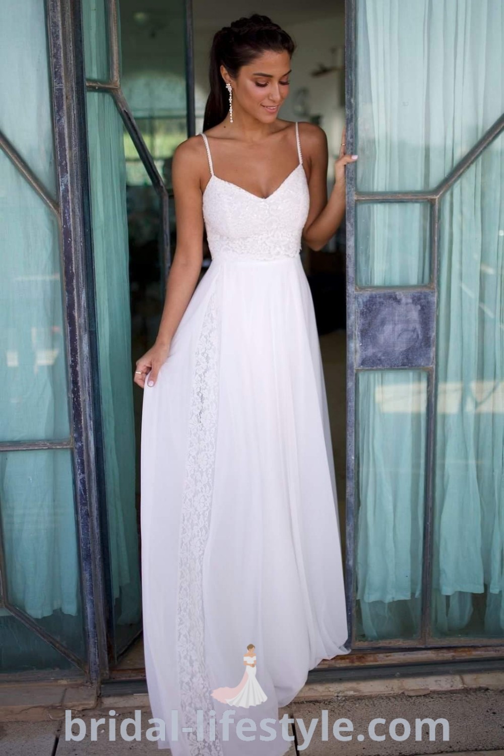 An elegant woman in a long white dress stands at an open door, showcasing a casual summer wedding dress perfect for beach or backyard weddings. This simple boho dress offers inspiration for every bride