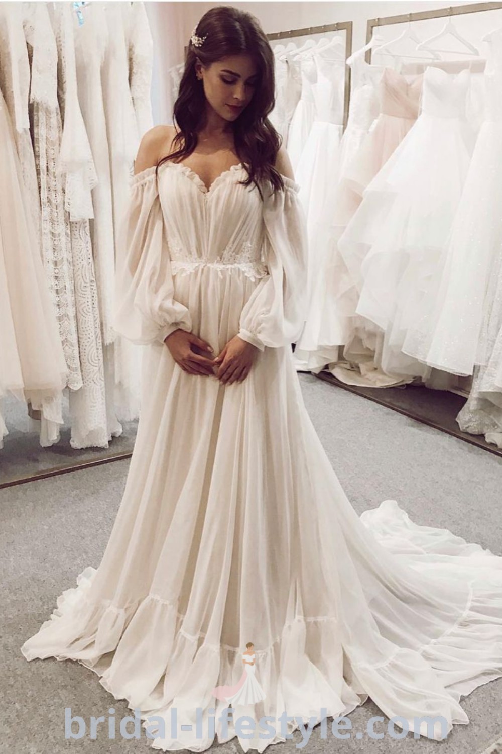 A woman standing in front of a rack of Mamma Mia inspired wedding dresses featuring elegant off-the-shoulder styles, floor-length designs, and beautiful buttons. A perfect selection for dreamy brides seeking inspiration looks for their special day at bridal-lifestyle.com.