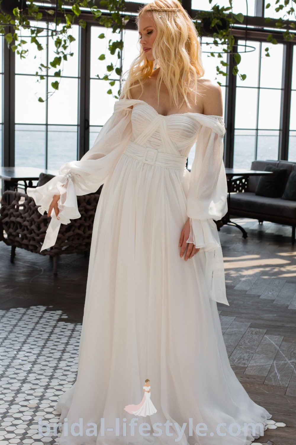 A woman in a white off-the-shoulder Boho wedding dress stands gracefully near a bench, embodying elegance and charm for dreamy brides. This flowy dress exemplifies the latest trends and is perfect for every bride