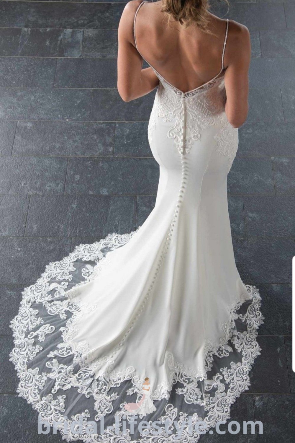 An elegant woman in a white Stella York wedding dress looks down at her back, showcasing the intricate lace detailing. This dreamy gown represents the best trends for brides, combining comfort and luxury. Explore more bridal inspirations at bridal-lifestyle.com.